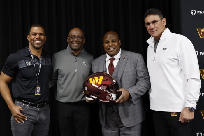 Eric Bieniemy (holding helmet) poses with (L-R) Washington Commanders team president Jason Wright, general manager Martin Mayhew, and head coach Ron Rivera.